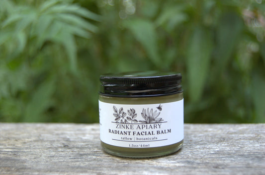 Jar of Zinke Apiary Radiant Facial Balm on a wooden surface with a blurred green background