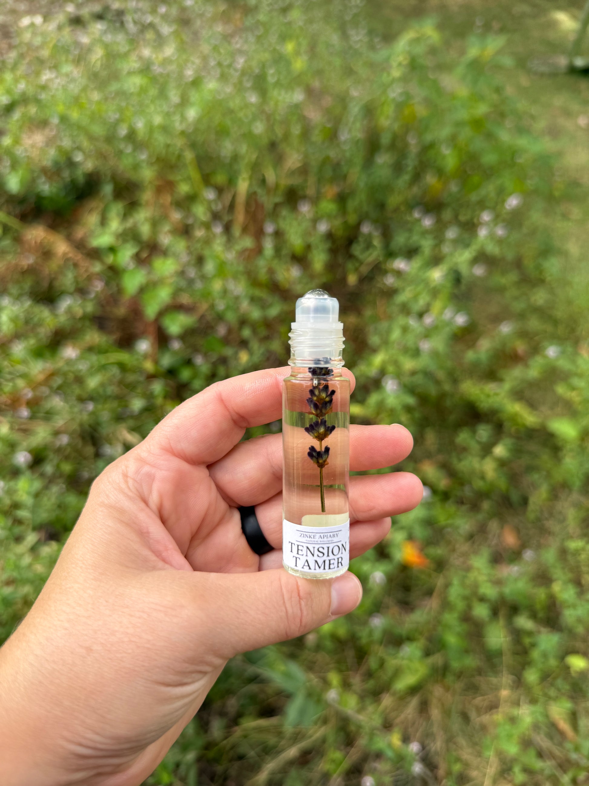 Hand holding a small bottle with a label against a blurred green outdoor background