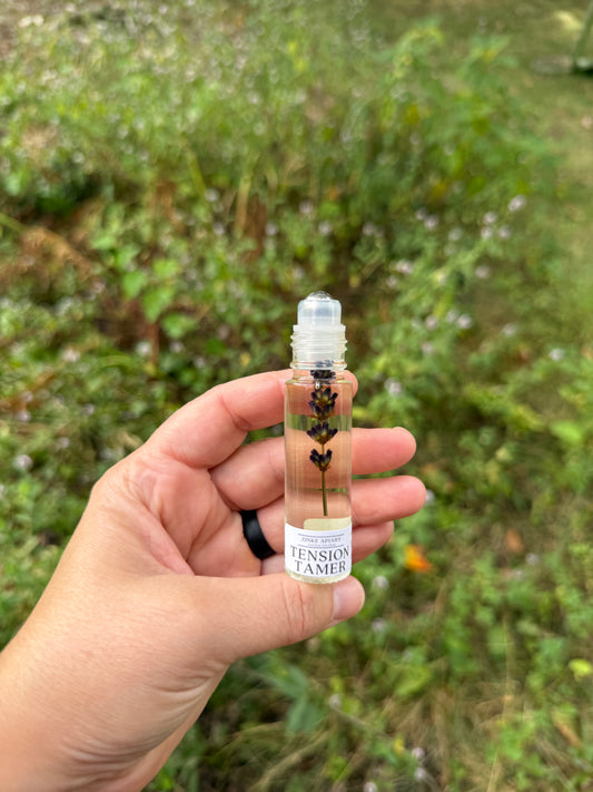 Hand holding a small bottle with a label against a blurred green outdoor background