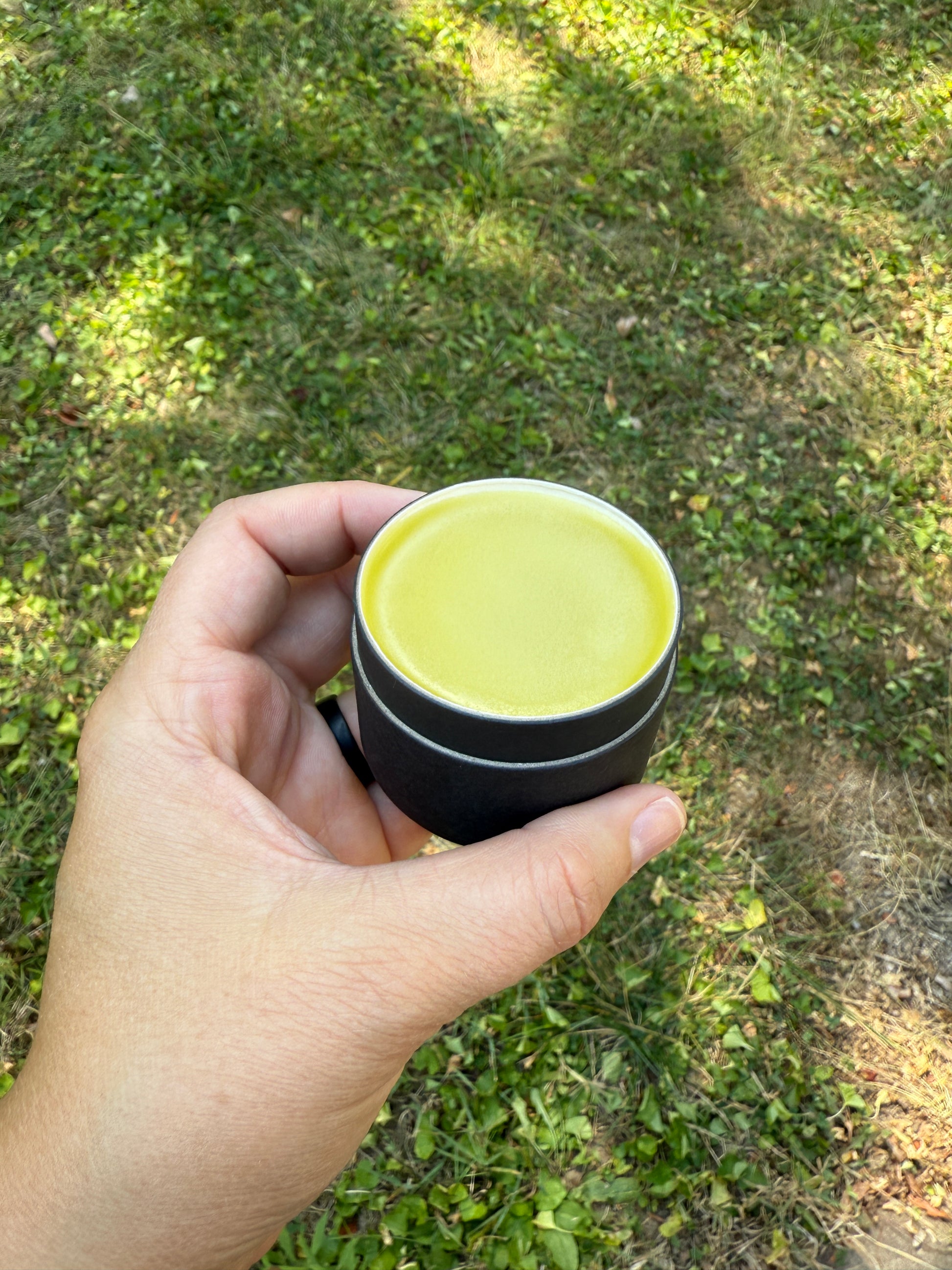 Hand holding a cylindrical container with a yellow lid outdoors on grass